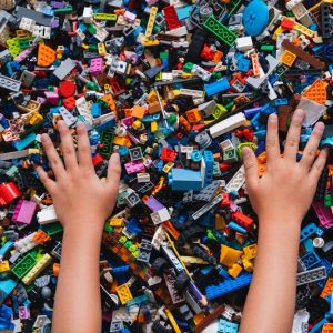 Huge pile of mixed colorful plastic bricks toys with children's hands. Small plastic building blocks in multiple colours, top view, lifestyle photo. Kids leisure, children education and development.